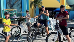 Een groep mensen op fietsen voor een gebouw met een bord waarop staat 'Ron Jon Surf Shop'.