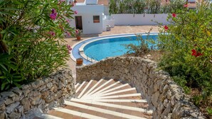 A stone staircase leading to a pool area with a white building in the background. - Apartment with a terrace and a view of the garden (Albufeira)