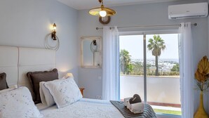 Una camera da letto con un letto grande, vista sulla città, un balcone con una palma e un condizionatore d'aria.