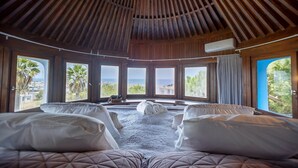 A room with a wooden ceiling, large windows, two beds with pillows, and a view of the sea. - Historic Windmill – Panoramic Views (Albufeira)