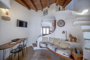 A cozy room with a curved sofa, a wooden table with chairs, a television, and a wall-mounted clock. - Historic Windmill – Panoramic Views (Albufeira)