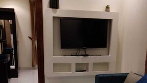 Una sala de estar con una televisión de pantalla plana montada en la pared, un sofá, una mesa de centro y piso de baldosas.