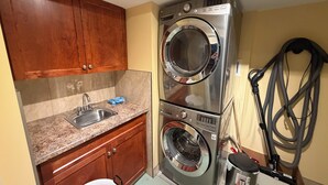 A compact laundry area with a sink, wooden cabinets, and stacked washer and dryer units. - Poolside Oasis in Penticton | Private Fenced Pool, 3BR Family Retreat (Penticton)