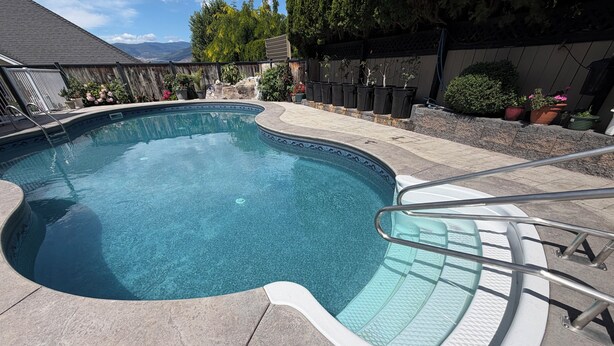 A swimming pool with a curved edge, a metal ladder, and a tiled deck. - Poolside Oasis in Penticton | Private Fenced Pool, 3BR Family Retreat (Penticton)