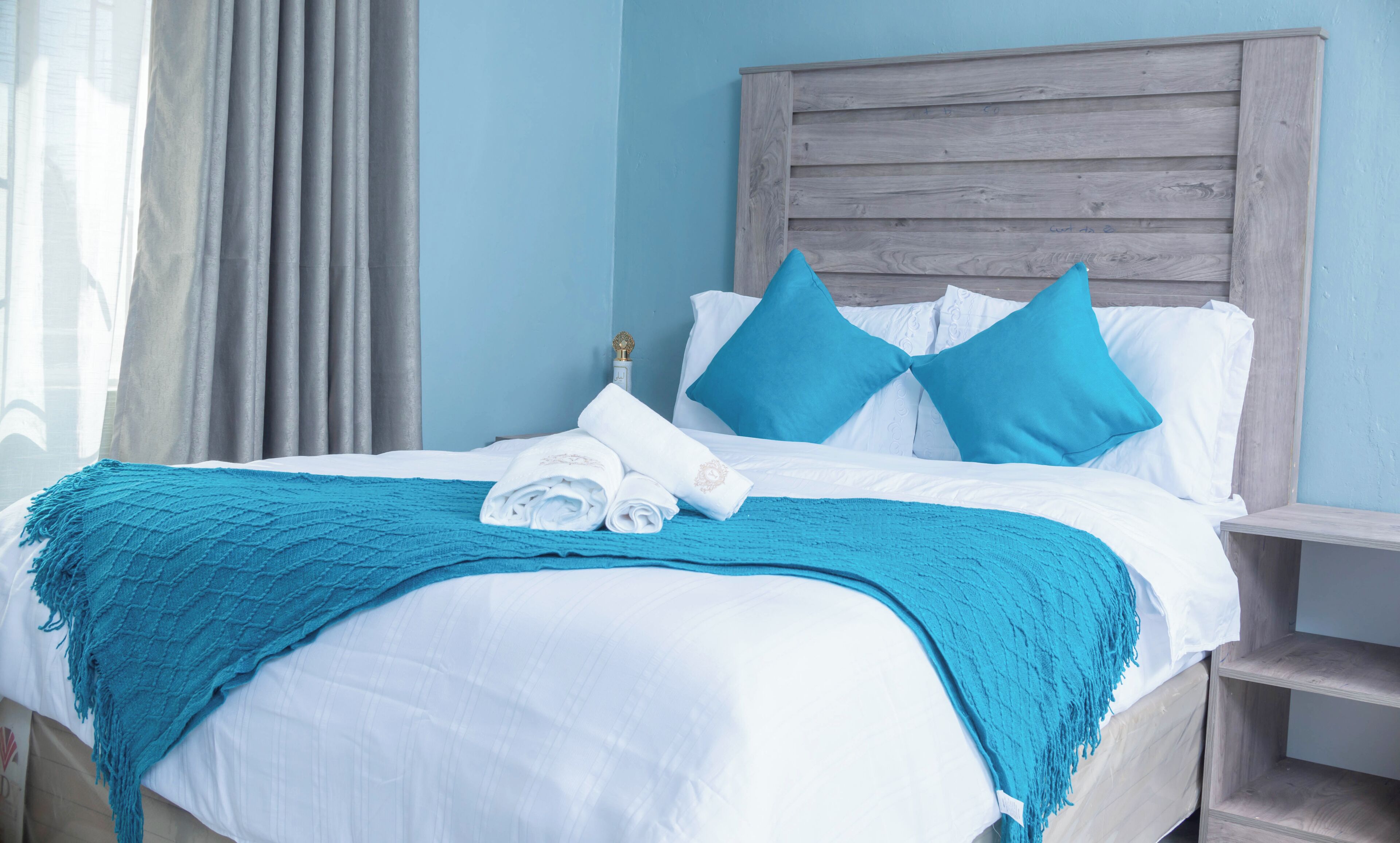 A neatly made bed with blue and white bedding, a blue throw blanket, and a wooden headboard.