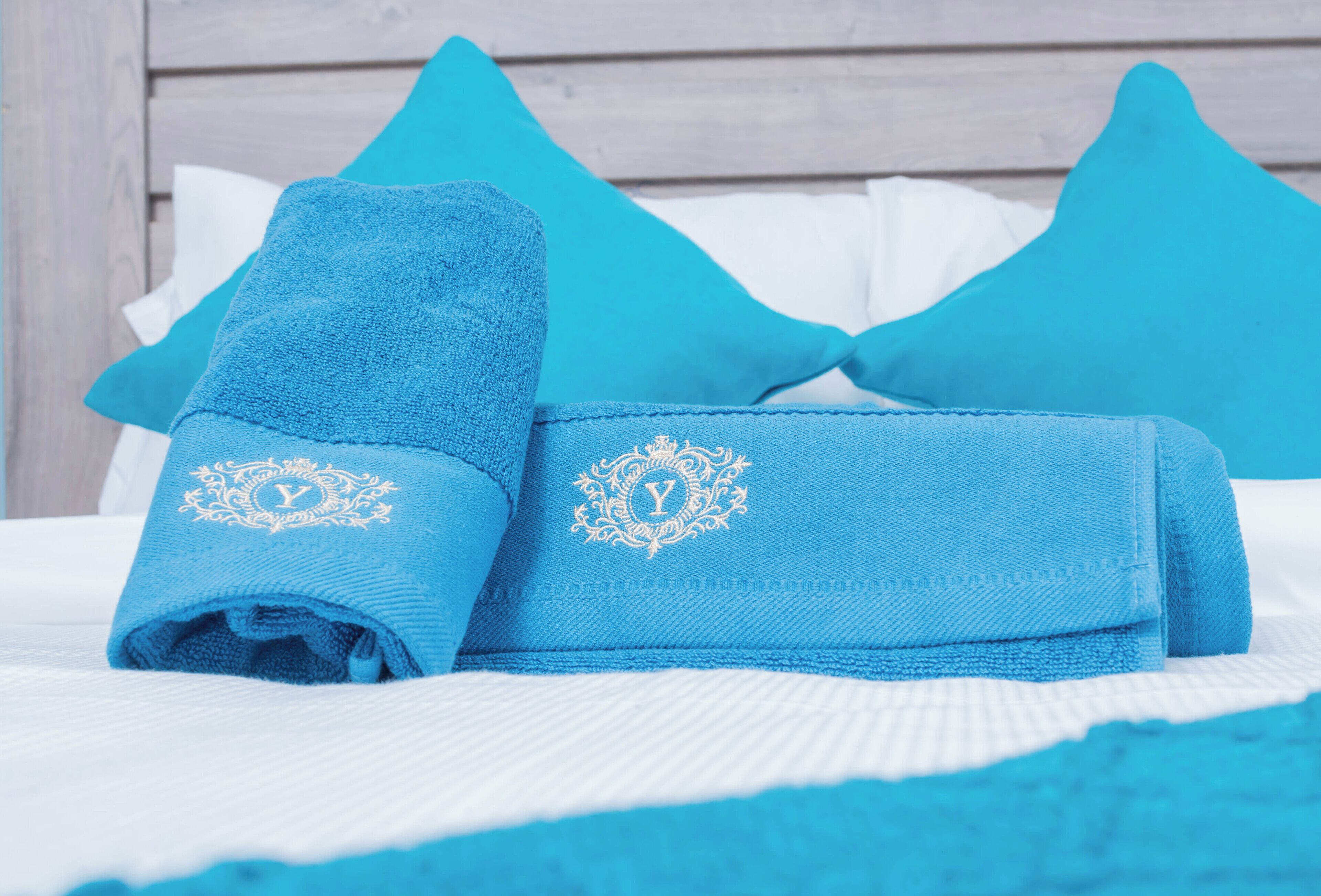 A neatly made bed with blue towels and pillows, a white bedspread, and a wooden headboard.