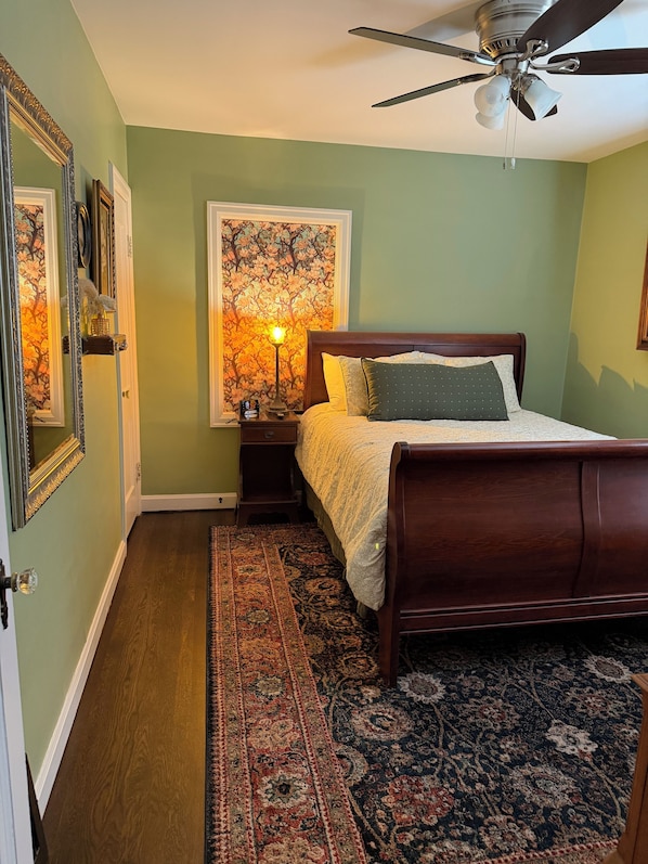 A bedroom with a bed, a nightstand, a lamp, a ceiling fan, and a large floral tapestry. - Charming Reilly Tudor Home in historic Leavenworth (Leavenworth)