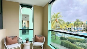 Ein Balkon mit zwei Stühlen, einem Deckenventilator und Blick auf einen Pool und Palmen.