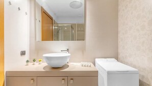 Un baño moderno con un lavamanos blanco grande, un espejo, una ducha y una lavadora integrada.