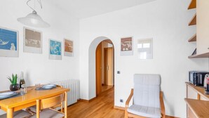 Un comedor con una mesa y sillas de madera, un sillón blanco, y un pasillo con un arco.