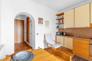 A compact kitchen with wooden cabinets, a microwave, and a chair. - CA2 [Loreto - Cathedral] • 10 minutes from the Duomo • (Milano)