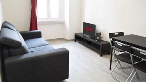 Un saló modern amb un sofà, una taula de dinar amb cadires, un televisor amb el logotip de Netflix i una finestra amb cortines vermelles.