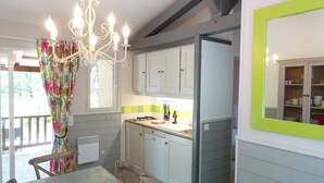 Ett kök med ett matbord, stolar, en kristallkrona, skåp och ett fönster med gardiner.