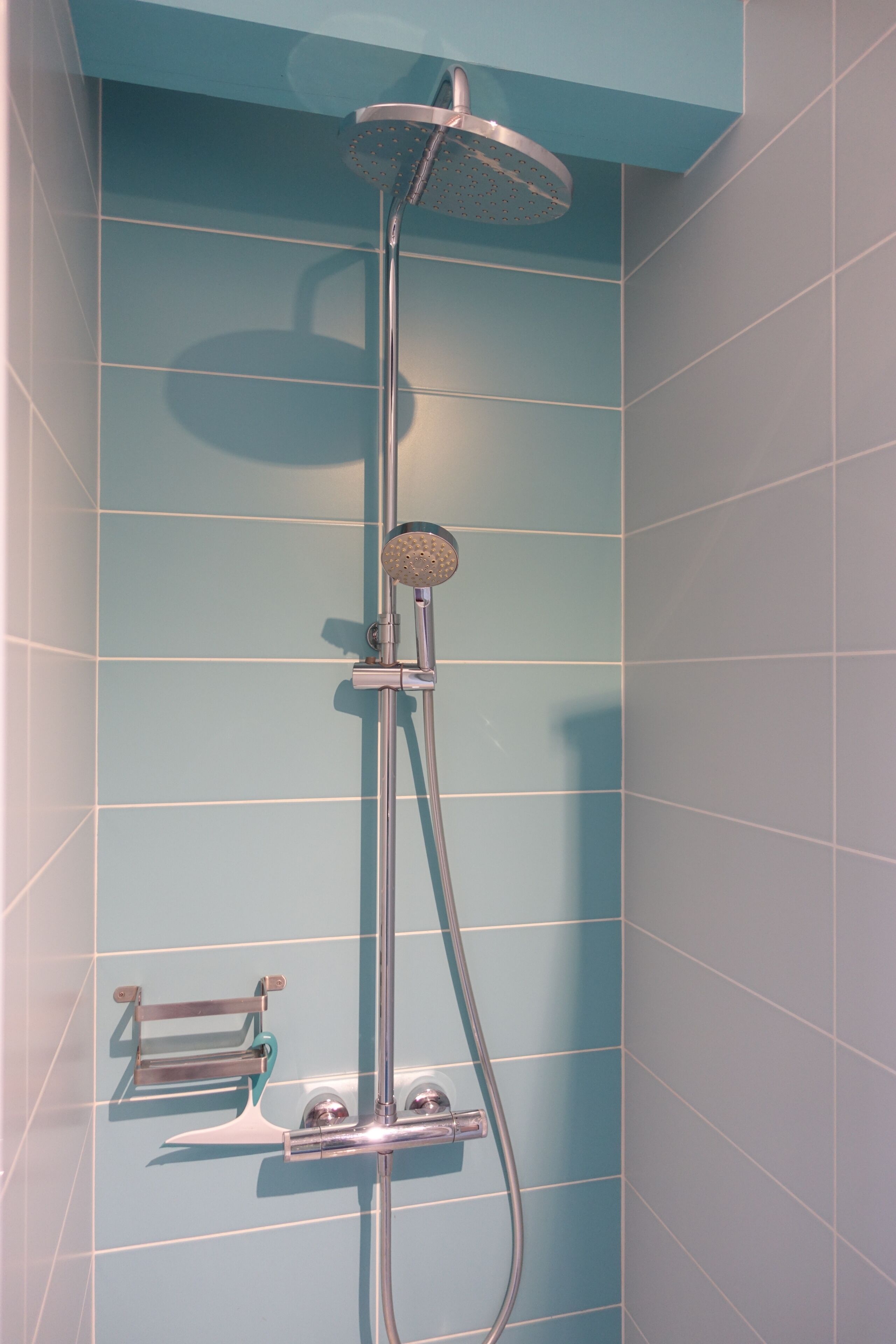 A shower with a handheld showerhead and a wall-mounted control panel.