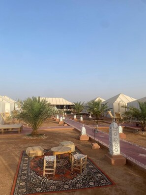 Un resort en el desierto con tiendas de campaña, palmeras y zonas de estar al aire libre.