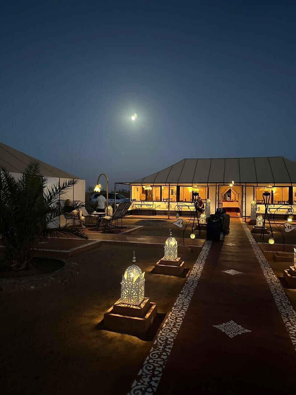 A building with a covered outdoor area, a pathway with decorative elements, and a person sitting at a table.