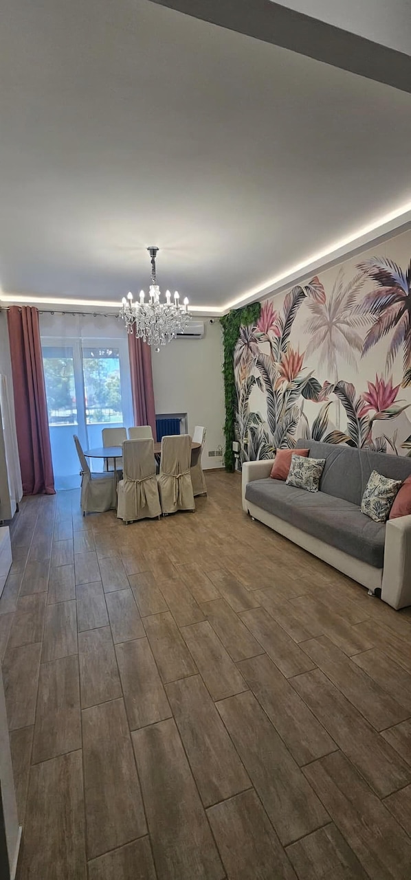 A modern living room with a sofa, chairs, a chandelier, a wall mural, and a dining area.