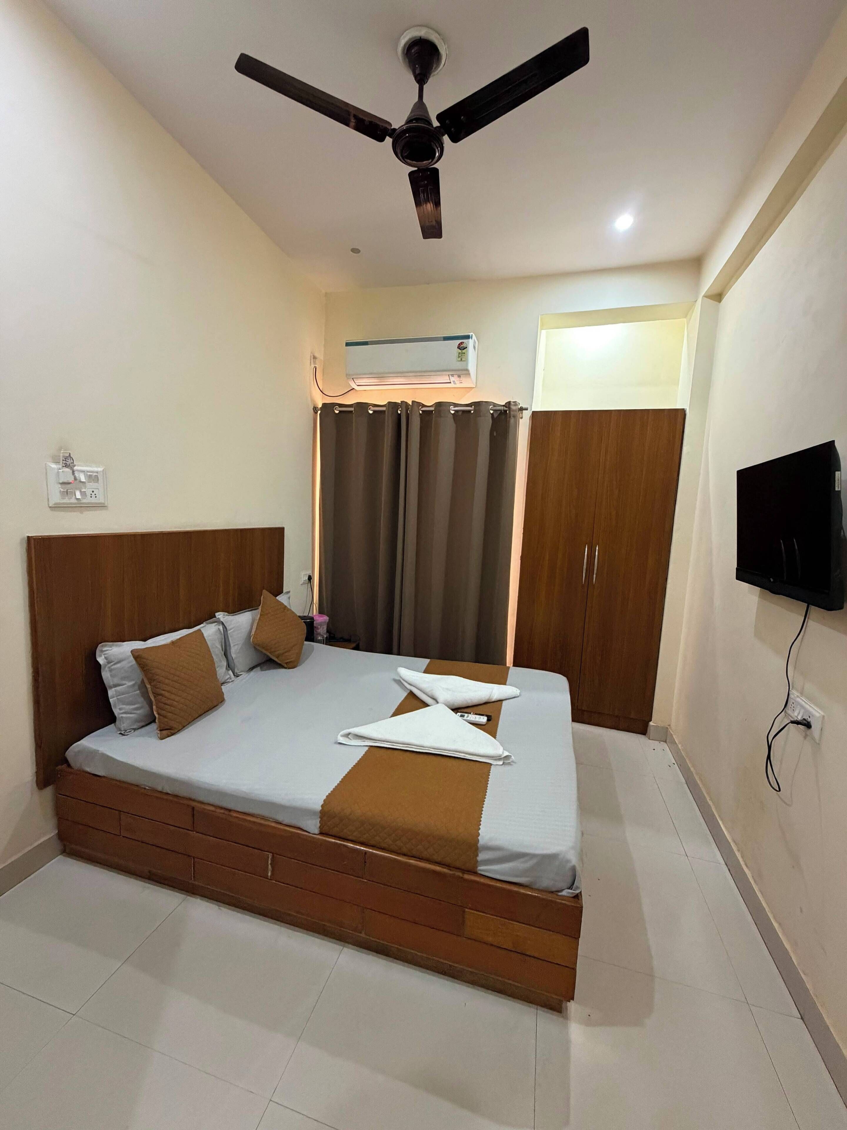 Una habitación de hotel con cama, ventilador de techo, aire acondicionado, televisión y armario.