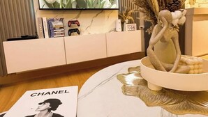 Ein modernes Wohnzimmer mit Marmorwand, Flachbildfernseher, Spielkonsole und einer dekorativen Vase mit Trockenpflanzen.