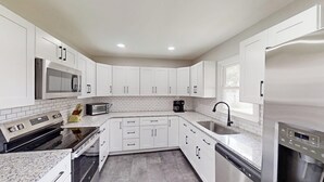 A modern kitchen with white cabinets, a microwave, a toaster, a coffee maker, a sink, and a dishwasher. - Fantastic 3-bedroom house charming Hays (Hays)