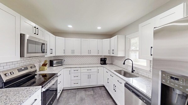 A modern kitchen with white cabinets, a microwave, a toaster, a coffee maker, a sink, and a dishwasher.