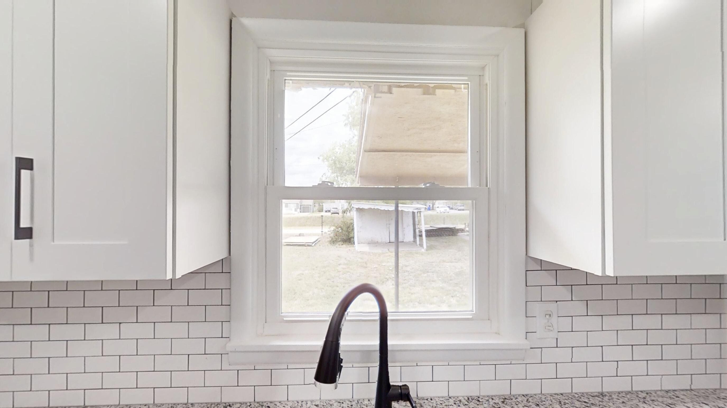 A kitchen with white cabinets, a window, and a tiled backsplash.