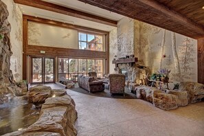 A spacious interior with a stone fireplace, large windows, and a view of the outdoors. - 1 Minute Walk to the Gondola/Shared Pool and Hot Tub/Private Patio (Keystone)