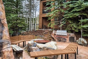 An outdoor patio with wooden benches, a barbecue grill, and a stone seating area surrounded by trees. - 1 Minute Walk to the Gondola/Shared Pool and Hot Tub/Private Patio (Keystone)