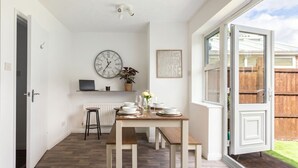 A dining area with a table set for two, a clock, a radiator, and a view of the outside. - 3-Bed House Sleeps 6 with Driveway Parking · 10 Min to Knutsford (Cheshire West and Chester)