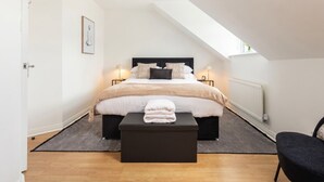 A bedroom with a bed, bedside lamps, a black ottoman, a framed picture on the wall, and a window providing natural light. - 3-Bed House Sleeps 6 with Driveway Parking · 10 Min to Knutsford (Cheshire West and Chester)
