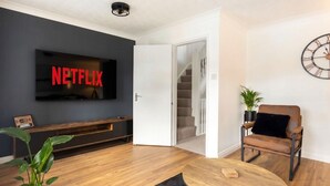 A living room with a flat-screen TV, a wooden coffee table, a leather armchair, a staircase, and a potted plant. - 3-Bed House Sleeps 6 with Driveway Parking · 10 Min to Knutsford (Cheshire West and Chester)