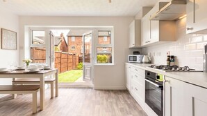 A modern kitchen with white cabinetry, a built-in oven, and a dining area with a table set for two. - 3-Bed House Sleeps 6 with Driveway Parking · 10 Min to Knutsford (Cheshire West and Chester)