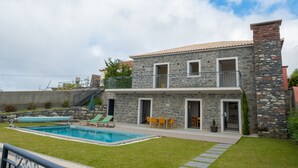 A two-story stone house with a swimming pool, outdoor seating, and a staircase leading to a balcony.