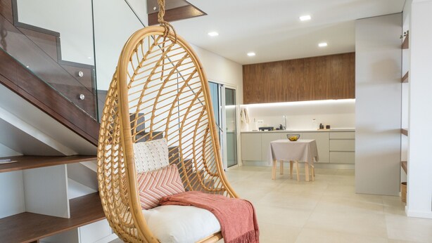 A modern interior with a hanging chair, a kitchen area, and a staircase.