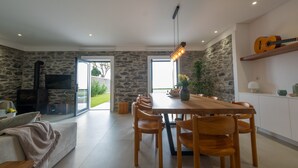 A modern living room with a stone wall, a fireplace, a dining area with wooden chairs, and a guitar on a shelf.