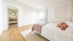 A modern bedroom with a large bed, a walk-in closet, and a bathroom with a circular mirror.