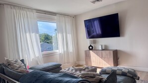 Olohuoneessa on sohva, rahi ja seinälle asennettu taulutelevisio.