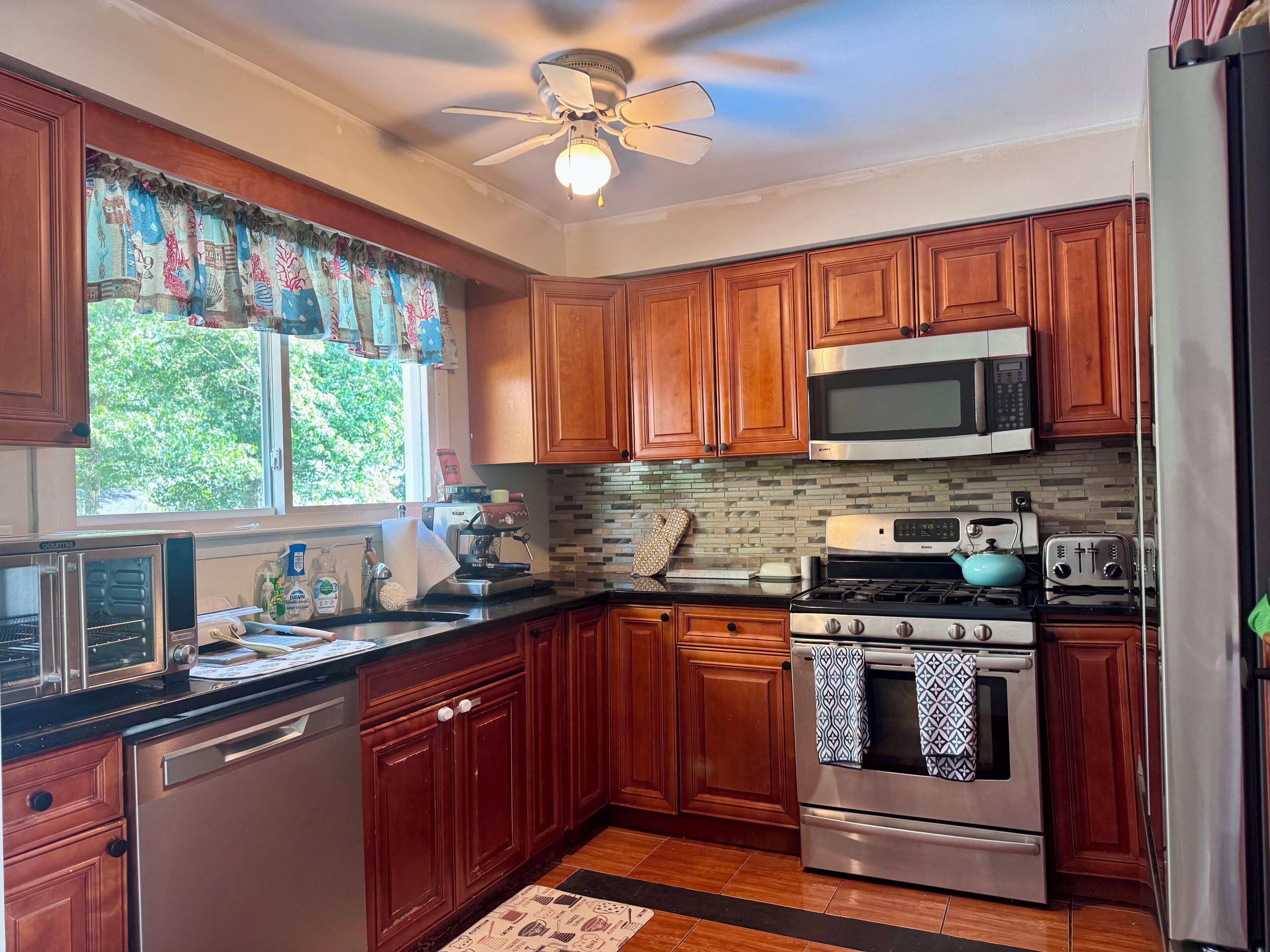 A kitchen with wooden cabinets, a microwave, a stove, and a ceiling fan.