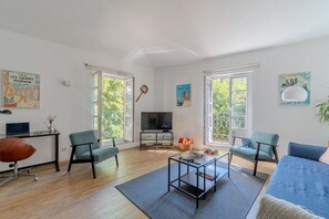 Ein modernes Wohnzimmer mit Fernseher, zwei grünen Sesseln, einem blauen Sofa und einem Couchtisch.