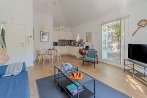 Ein modernes Wohnzimmer mit Sofa, Glastisch, Fernseher und Küchenzeile.