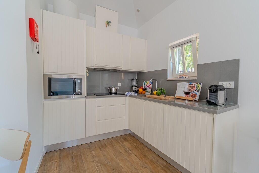 A modern kitchen with white cabinets, a microwave, a kettle, and a window with a view of greenery.