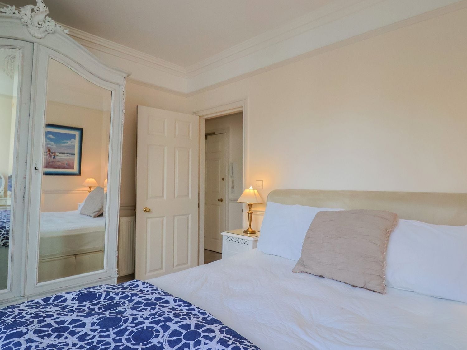 Un dormitorio con cama, mesita de noche, lámpara, espejo y una puerta.