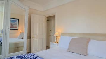 Un dormitorio con cama, mesita de noche, lámpara, espejo y una puerta.