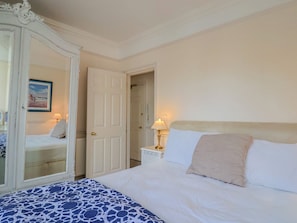 A bedroom with a bed, a nightstand, a lamp, a mirror, and a door. - 2 St Michaels House (Lyme Regis)