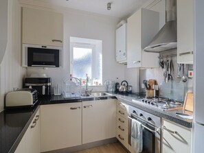 Uma cozinha moderna com armários brancos, micro-ondas, torradeira, chaleira e fogão a gás.
