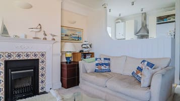 Una sala de estar con chimenea, un sofá con cojines decorativos, una lámpara y un cuadro en la pared.