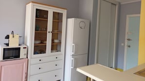 Una cocina con microondas, un mueble con puertas de vidrio, un refrigerador y una puerta con picaporte.