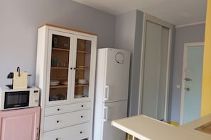 Eine Küche mit Mikrowelle, einem Schrank mit Glastüren, einem Kühlschrank und einer Tür mit Griff.
