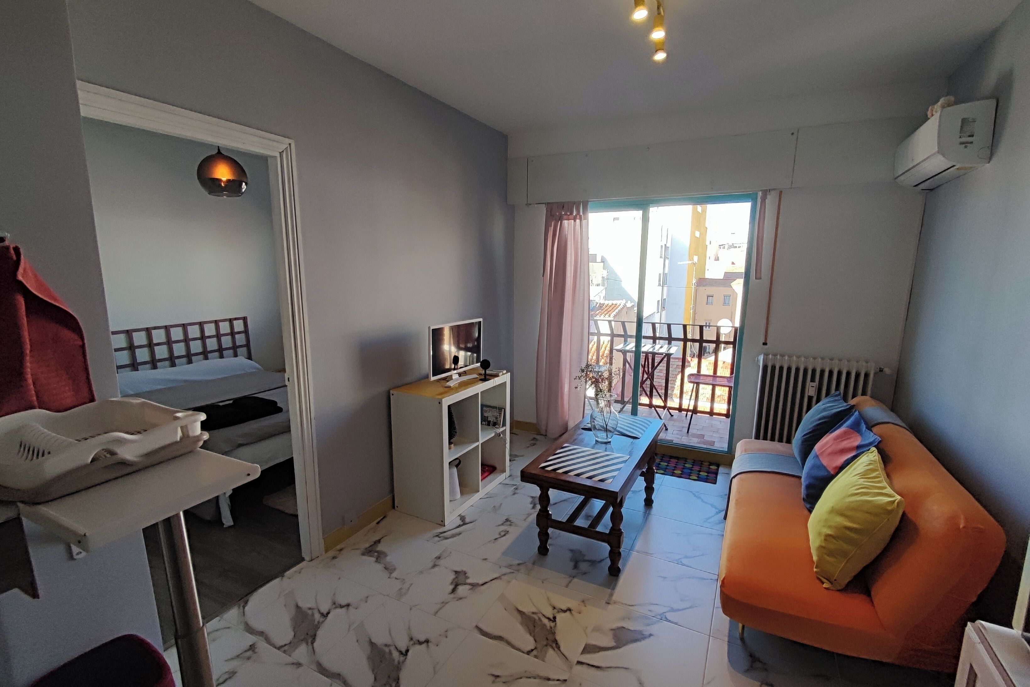 Ein Zimmer mit einem Bett, einem kleinen Tisch, einer Couch, einem Heizkörper und einem Fenster mit Blick auf Gebäude.