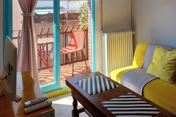 A room with a yellow sofa, a wooden coffee table with striped cushions, a red chair, and a large window with a view of a patio area. - Madrid Salamanca • Bright apartment with a terrace (Madrid)